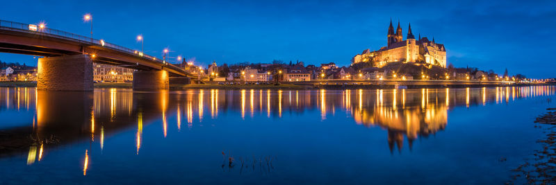 Illuminated buildings by river against sky at night