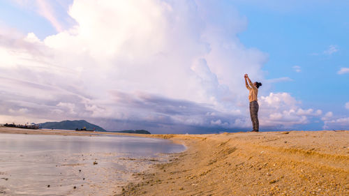 Woman photographing at beach against sky