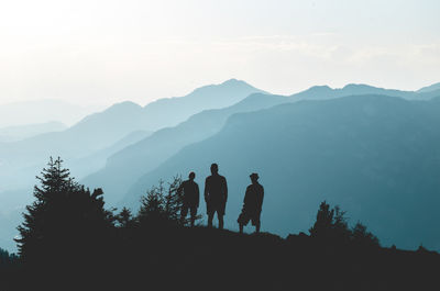 Silhouette friends standing by mountains against sky in foggy weather