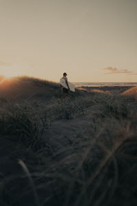 Man sitting on field against sky during sunset