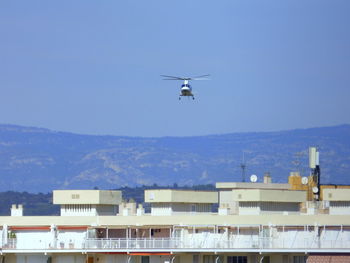 Helicopter flying over buildings against clear sky