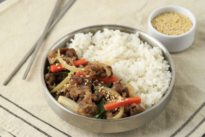 Korean beef bulgogi with stir fry vegetable over white rice, served on stainless bowl