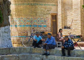 Group of people sitting by stone wall