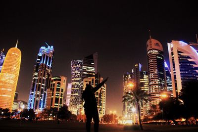 Full length of man standing by illuminated buildings against sky at night