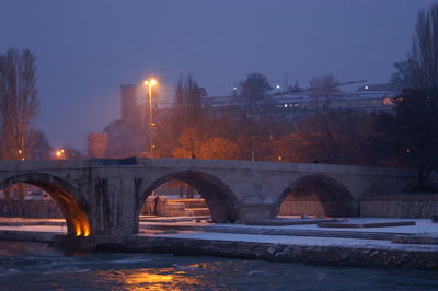 Illuminated bridge over river against clear sky at night