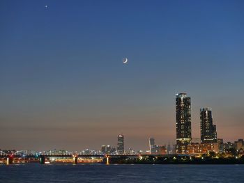 Illuminated city by sea against sky at night