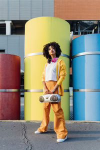 Young woman holding boom box standing in front of colorful pipes