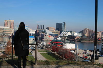 Rear view of woman standing by cityscape against clear sky