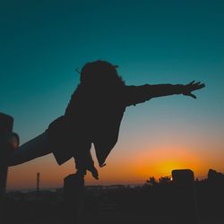 Silhouette woman with arms outstretched against sky during sunset