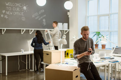 Young businessman talking on smart phone while female colleagues working by wall at creative office