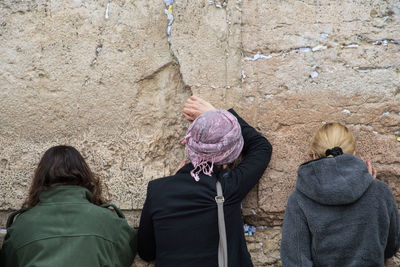 Rear view of women wearing warm clothing while standing against wall
