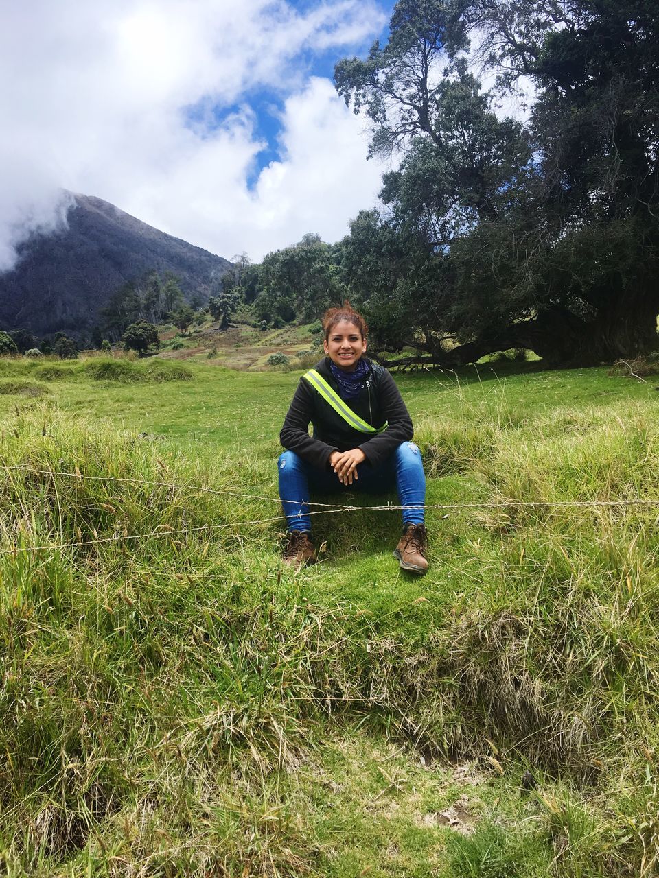 plant, real people, grass, one person, land, field, leisure activity, lifestyles, casual clothing, nature, full length, young adult, looking at camera, green color, portrait, mountain, front view, sitting, day, outdoors