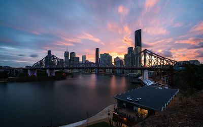 Illuminated bridge over river by buildings against sky during sunset
