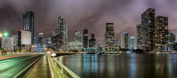 Illuminated buildings by river against sky in city at night