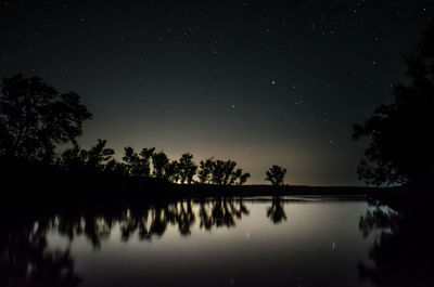 Silhouette trees by lake against sky at night