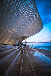 People walking on footpath by sea against sky