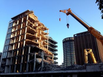 Low angle view of crane by building against clear sky