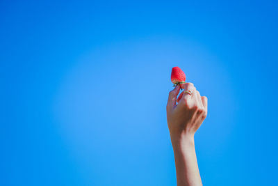 Midsection of person holding strawberry against clear blue sky