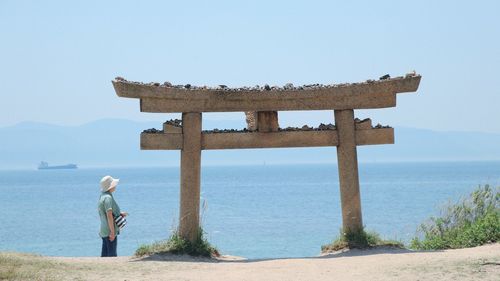 Rear view of woman standing by sea against clear sky