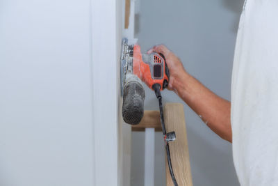 Midsection of man holding sander on wall