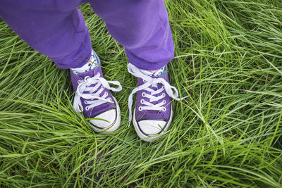 Girl wearing purple pants and shoes standing in long green grass