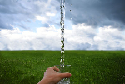 Close-up of hand holding stick on field against sky