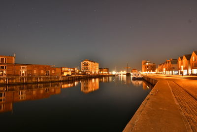 Illuminated buildings by river against sky in city at night