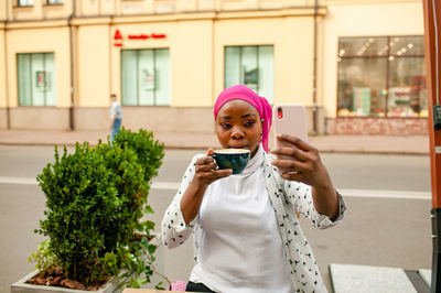 Portrait of young woman using mobile phone in city