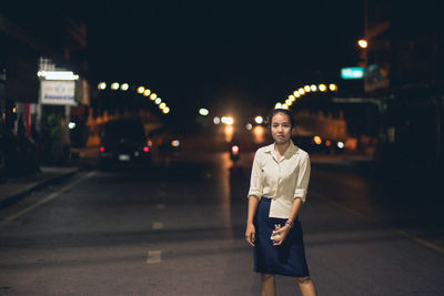 Portrait of teenage girl standing on road at night