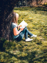 Young woman reading a book while sitting on field