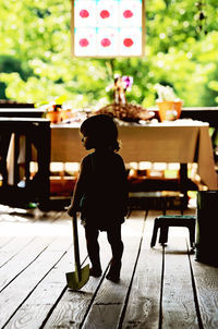 Rear view of baby girl holding shovel while walking on floorboard