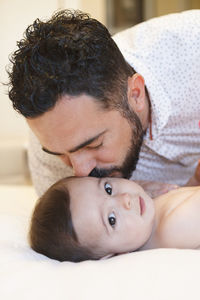 Father kissing cute baby boy lying on bed