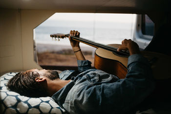 Man playing guitar while lying down on bed