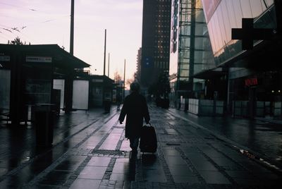 Rear view of woman walking on wet street in city