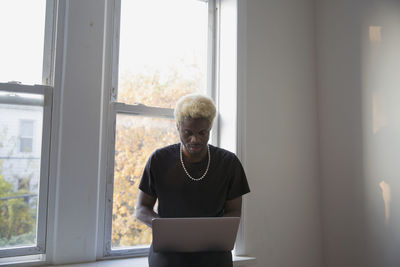 A young man with a laptop sitting on a window sill