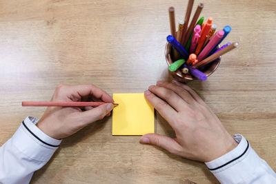 High angle view of hand writing on adhesive note over table