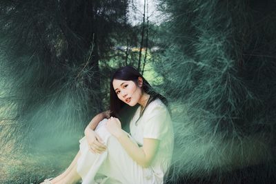 Portrait of beautiful woman sitting against trees in forest