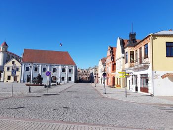 Road amidst buildings in town against clear blue sky