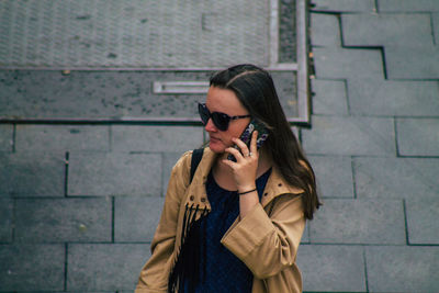 Portrait of woman wearing sunglasses standing against brick wall