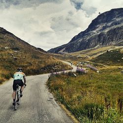 Rear view of man cycling on mountain road against sky