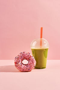 Donut and matcha in plastic cup on pink background