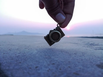 Cropped hand holing locket at beach against sky