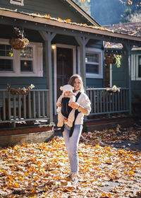 A woman with a child is standing near a house on yellow leaves