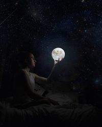Young woman holding glowing moon globe in dark