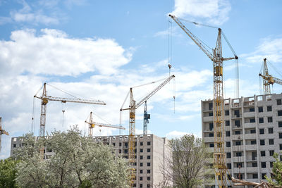 Low angle view of cranes against buildings in city