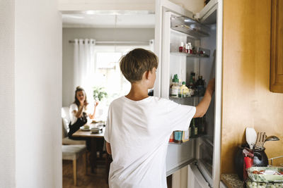 Pre-adolescent boy opening refrigerator door while standing in kitchen
