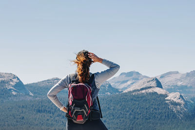 Woman with a backpack looking on the mountains after the hike to the top, view from the back