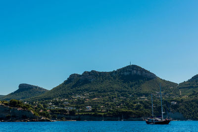 Boats sailing on sea by mountains against clear blue sky