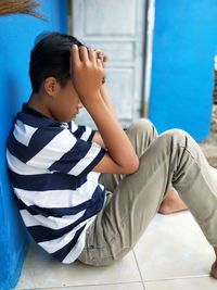 Rear view of boy sitting against blue wall