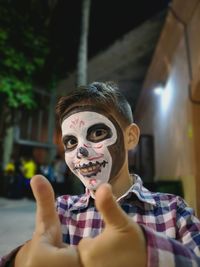 Portrait of boy with face paint showing thumbs up sign at night